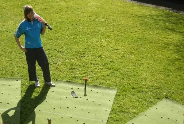 Cricket Coaching Mat featured outdoors on grass, with practice pegs and holes; player holding bat, ideal for cricket training.