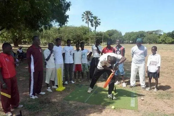 Children and adults use our Cricket Coaching Mat outdoors, with yellow stumps and cricket equipment—perfect for practice sessions.