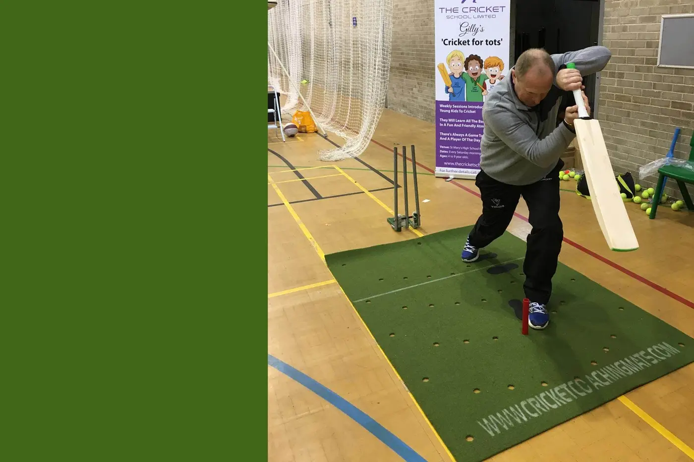 Man uses Cricket Coaching Mat indoors, surrounded by cricket kit, "Cricket for Tots" banner, nets, and solid green display area.