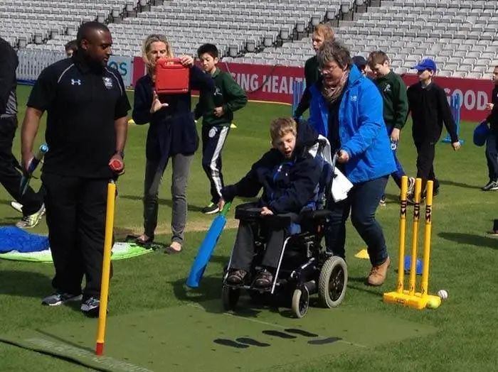 A boy in a wheelchair plays cricket on our Cricket Coaching Mat, assisted by staff and coach, showing inclusivity and adaptive equipment.