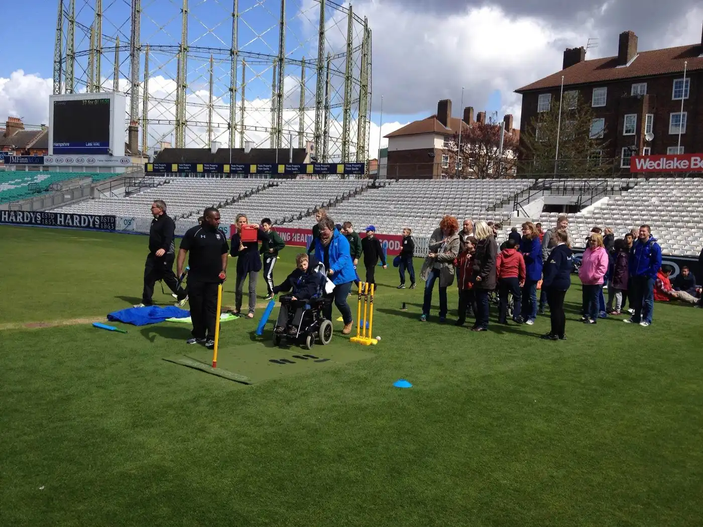 Inclusive cricket session using our Cricket Coaching Mat on grass, with players (including wheelchair user) and spectators nearby.