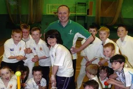 Children in white kits and a coach smile indoors with our Cricket Coaching Mats and cricket training equipment in the background.